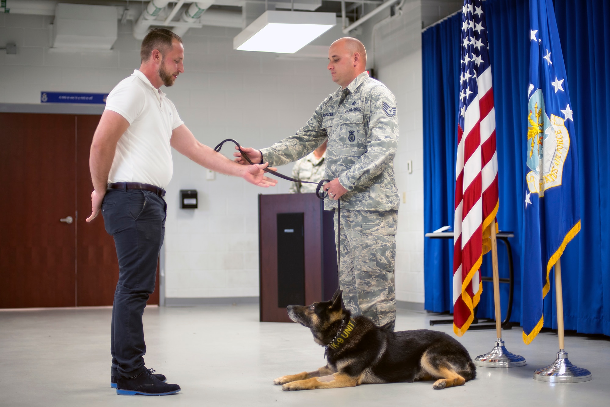 U.S. Air Force Staff Sgt. Matthew McElyea, a military working dog trainer, hands off the leash and the responsibility of taking care of Apacs to his new adopter Brandon Denton, a former military working dog handler, March 9, 2018, at MacDill Air Force Base, Fla. Denton was Apacs handler for the first three years of his service.
