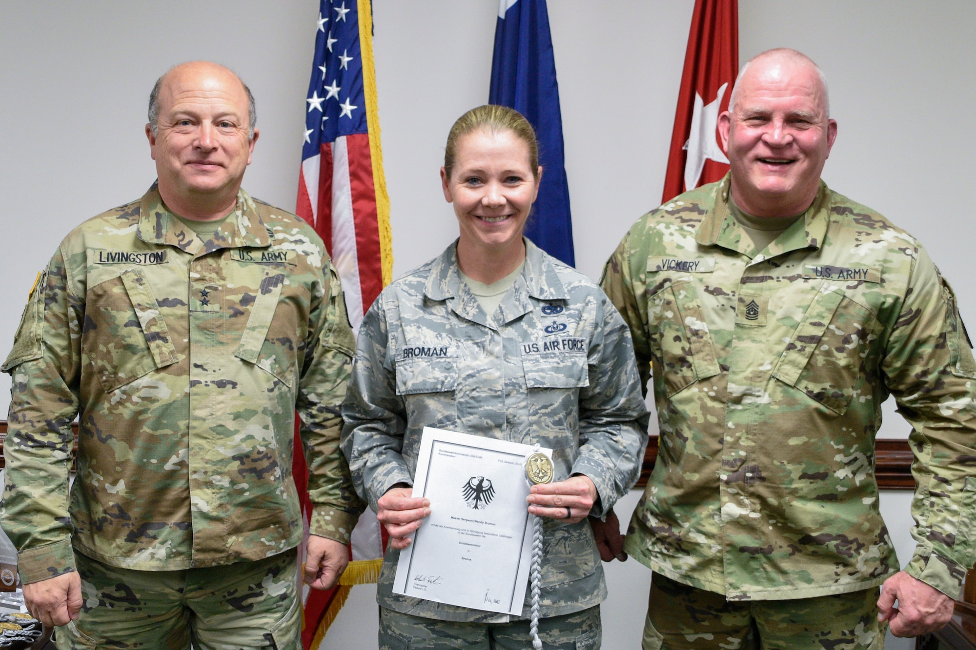 U.S.Army Maj. Gen. Robert E. Livingston Jr., adjutant general for South Carolina and State Command Sgt. Maj. Russel A. Vickery present the Schutzenschnur Badge to Master Sgt. Wendy Broman, a financial management specialist assigned to the South Carolina Air National Guard's 169th Fighter Wing, for demonstrating profeciency in firing German weapons at a ceremony March 7, 2018 at the Adjutant Generals' building in Columbia S.C. Broman and several other service members were chosen to participate in a specialized training opportunity to work with German soldiers. They learned how to fire a German rifle, pistol and machine gun. (U.S. Army National Guard photo by 1st Lt. Tracci Dorgan)
