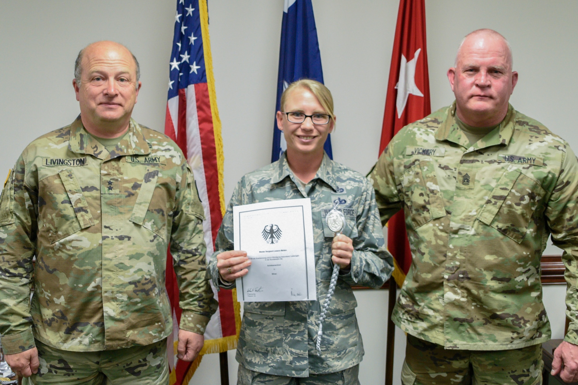 U.S.Army Maj. Gen. Robert E. Livingston Jr., adjutant general for South Carolina and State Command Sgt. Maj. Russel A. Vickery present the Schutzenschnur Badge to Master Sgt. Leeann Melton, a paralegal assigned to the South Carolina Air National Guard's 169th Fighter Wing, for demonstrating profeciency in firing German weapons at a ceremony March 7, 2018 at the Adjutant Generals' building in Columbia S.C. Melton and several other service members were chosen to participate in a specialized training opportunity to work with German soldiers. They learned how to fire a German rifle, pistol and machine gun. (U.S. Army National Guard photo by 1st Lt. Tracci Dorgan)