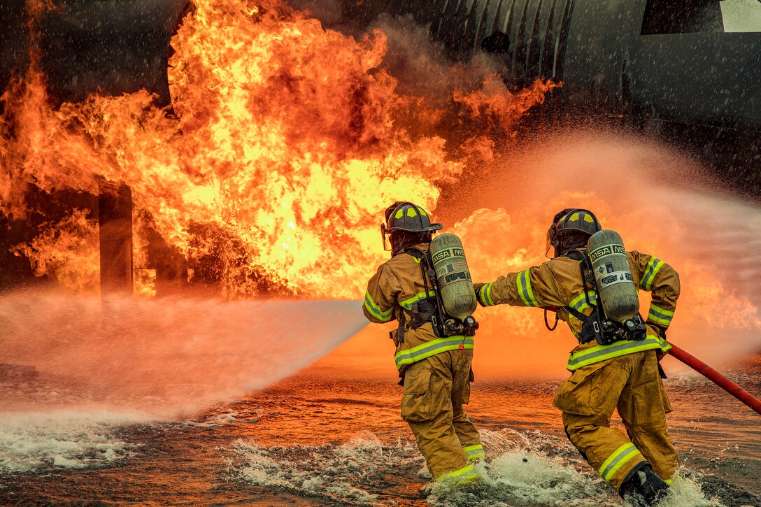 Two firefighters spray flames with a hose.