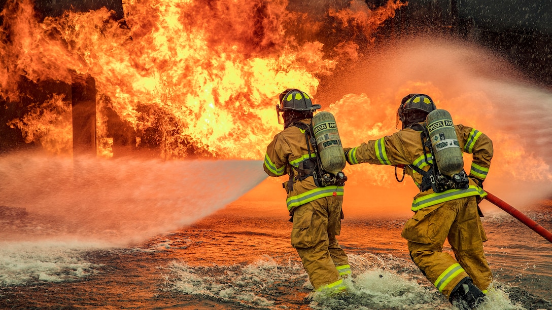 Two firefighters spray flames with a hose.