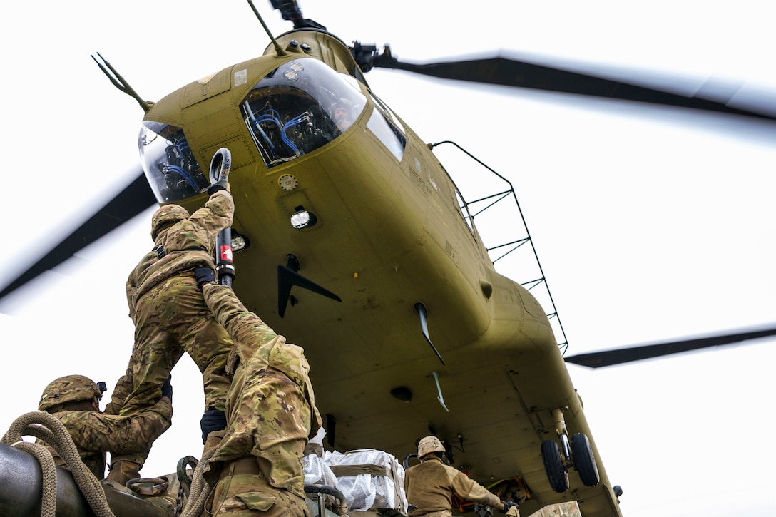 A helicopter hovers above a solider holding up a sling as he's lifted by fellow soldiers.
