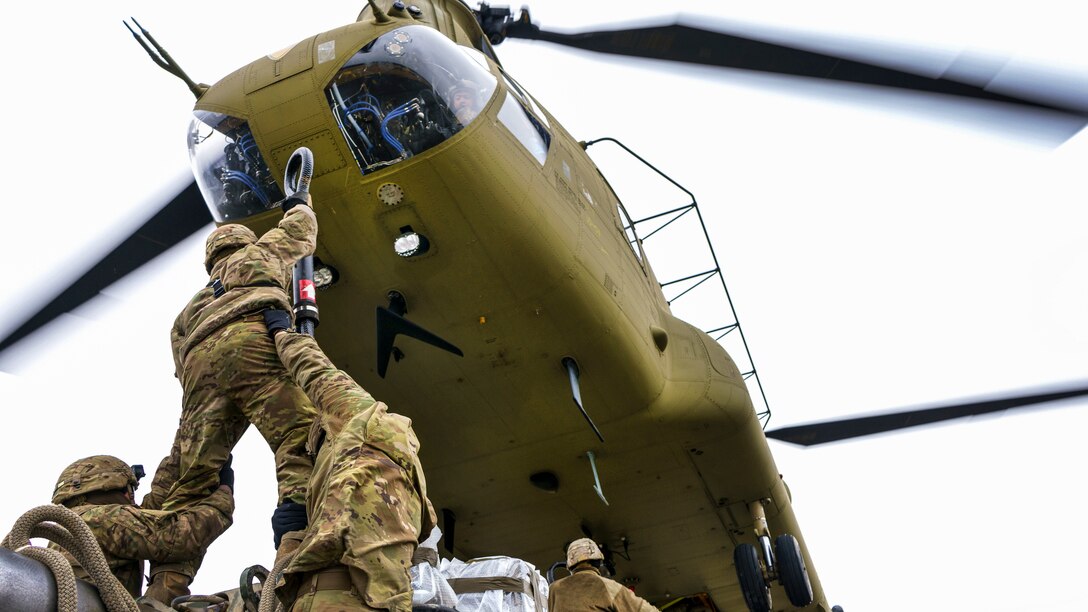 A helicopter hovers above a solider holding up a sling as he's lifted by fellow soldiers.