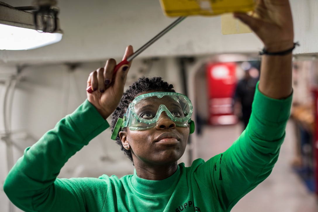 A sailor uses a tool to test a battle lantern on a ship.