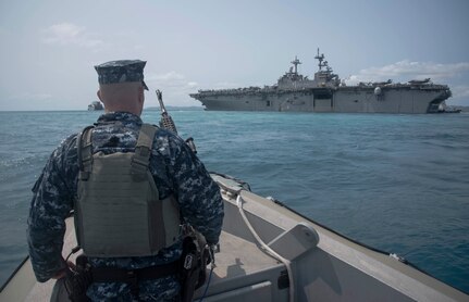 180319-N-YG104-0039 OKINAWA, Japan (March 19, 2018) Master-at-Arms 2nd Class Thomas Butcher looks on from a harbor patrol boat as the amphibious assault ship USS Wasp (LHD 1) departs the harbor at White Beach Naval Facility. Wasp, with embarked 31st Marine Expeditionary Unit, is operating in the Indo-Pacific region as part of a regularly scheduled patrol and provides a rapid-response capability in the event of a regional contingency or natural disaster. (U.S. Navy photo by Mass Communication Specialist 2nd Class Sarah Villegas/ Released)