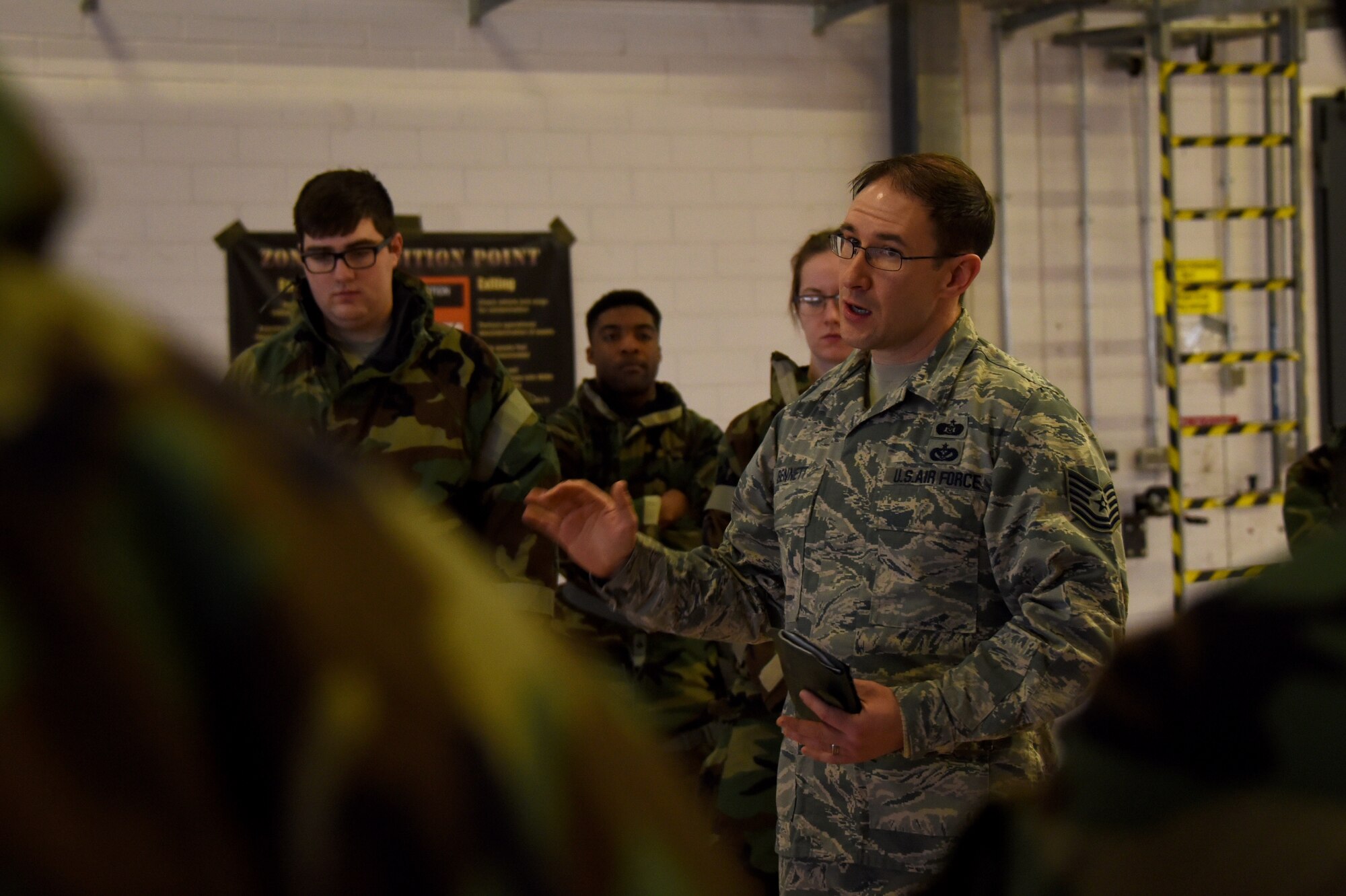 U.S. Air Force Tech. Sgt. Timothy Bennett, 52nd Civil Engineer Squadron emergency management craftsman, briefs Airmen assigned to the 52nd Fighter Wing about Mission-Oriented Protective Posture gear and levels during Ability to Survive and Operate training at Spangdahlem Air Base, Germany, March 8, 2018. In an effort to advance combat readiness the 52nd FW conducted a base-wide readiness exercise March 6 – 15. (U.S. Air Force photo by Senior Airman Dawn M. Weber)