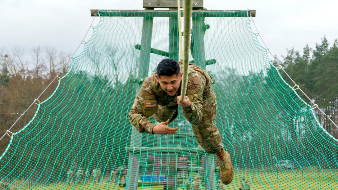 A soldier moves down a rope above a green net.