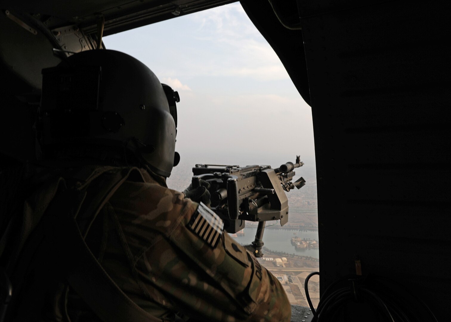 Gunner mans his post at the open door of a helicopter in flight.