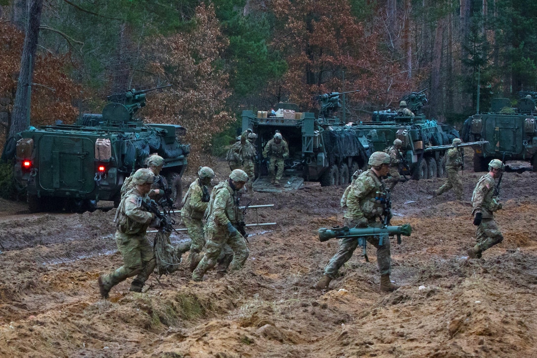 Soldiers run across a muddy field.