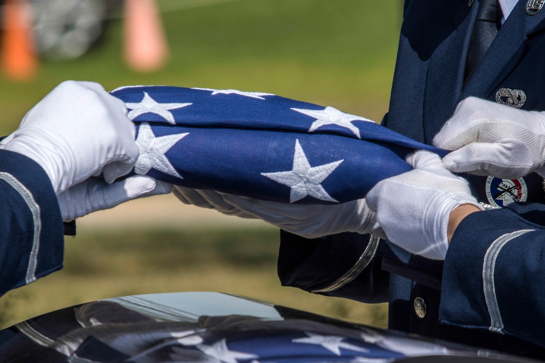 The white-gloved hands of three airmen hold a folded American flag over a casket.