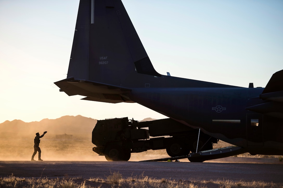 An airman uses hand signals to offload an artillery rocket system.