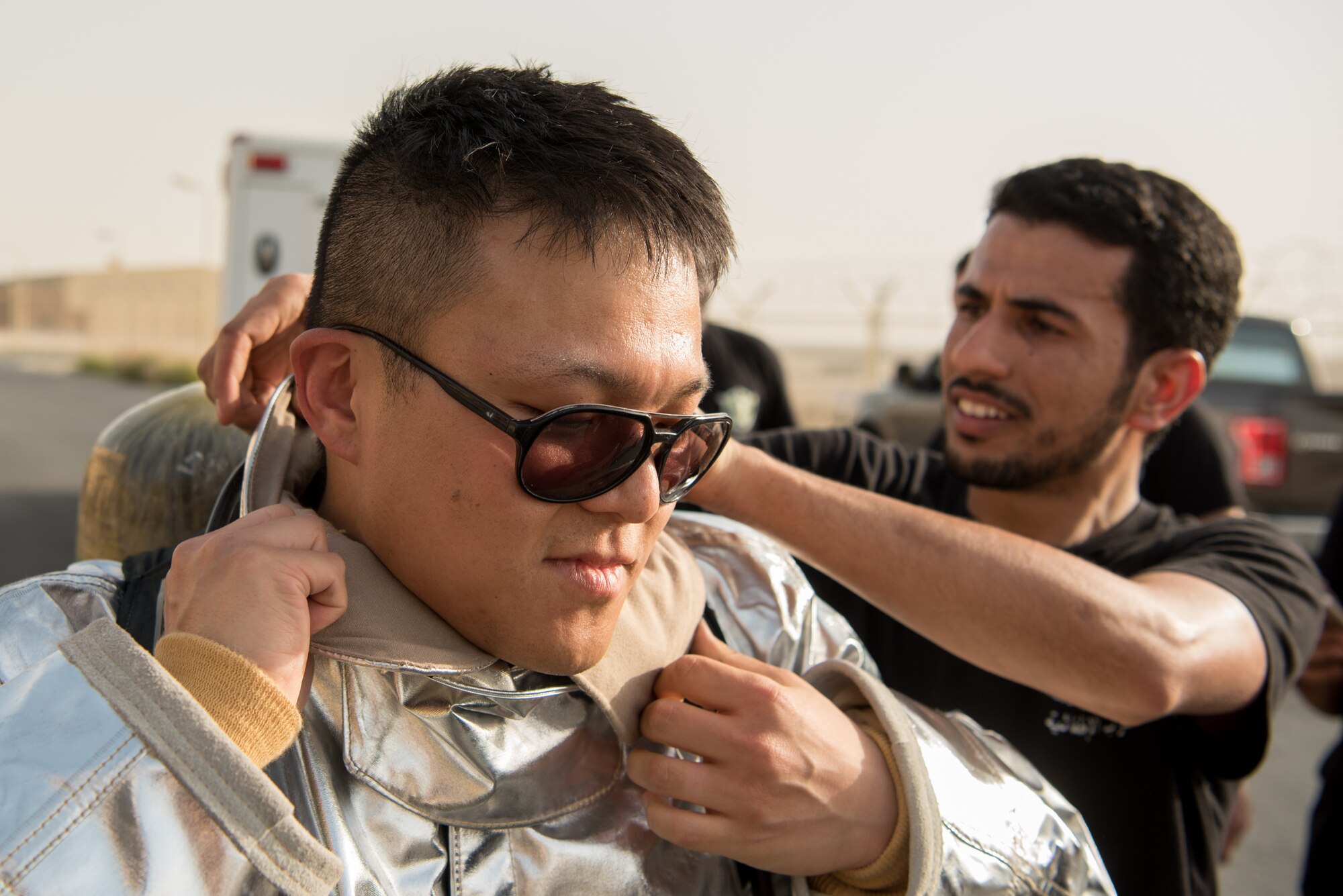 2nd Lt. Taegyung Lee (left), project manager from the 379th Expeditionary Civil Engineer Squadron, is assisted by a firefighter from the Qatar Emiri Air Force as Lee prepares to participate in a firefighter challenge exercise at Al Udeid Air Base, Qatar, March 8, 2018. The a exercise, a strenuous course designed to test physical fitness and fire response capabilities, was organized by firefighters from the 379th ECES and QEAF. (U.S. Air Force photo by Staff Sgt. Joshua Horton)