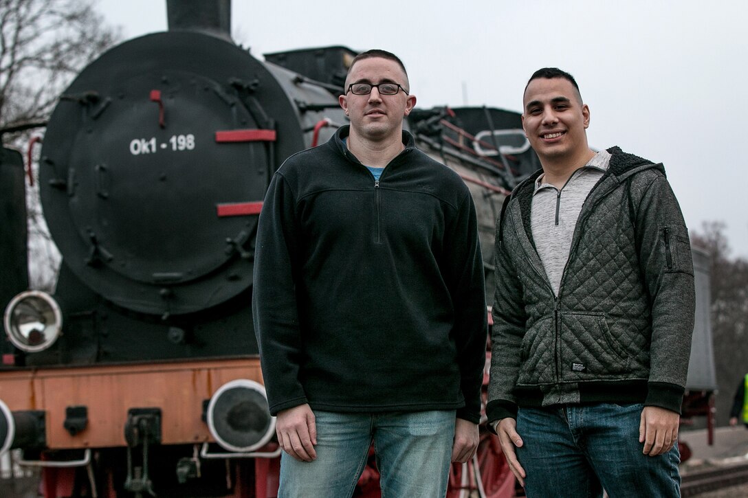 Two airmen pose for a photo in front of a train in Poland.