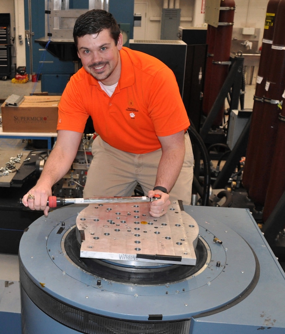 IMAGE: DAHLGREN, Va. - Naval Surface Warfare Center Dahlgren Division (NSWCDD) engineer Shawn Schneider mounts an adapter plate to an Unholtz-Dickie T-2000 electro-dynamic vibration system capable of providing over 24,000 pounds of force in vibration at frequencies up to and exceeding 3,000 hertz (cycles per second). These systems are used to replicate shock and vibration environments experienced by test items during their lifecycle to ensure that performance and safety are not compromised prior to use by the warfighter. NSWCDD announced on March 20 that Schneider won the 2018 Department of the Navy Award for Technical Excellence at a Test and Evaluation Facility or Range. The engineer was honored for extraordinary scientific and engineering contributions to the test and evaluation community in the area of multi-input-multi-output vibration test profiles.