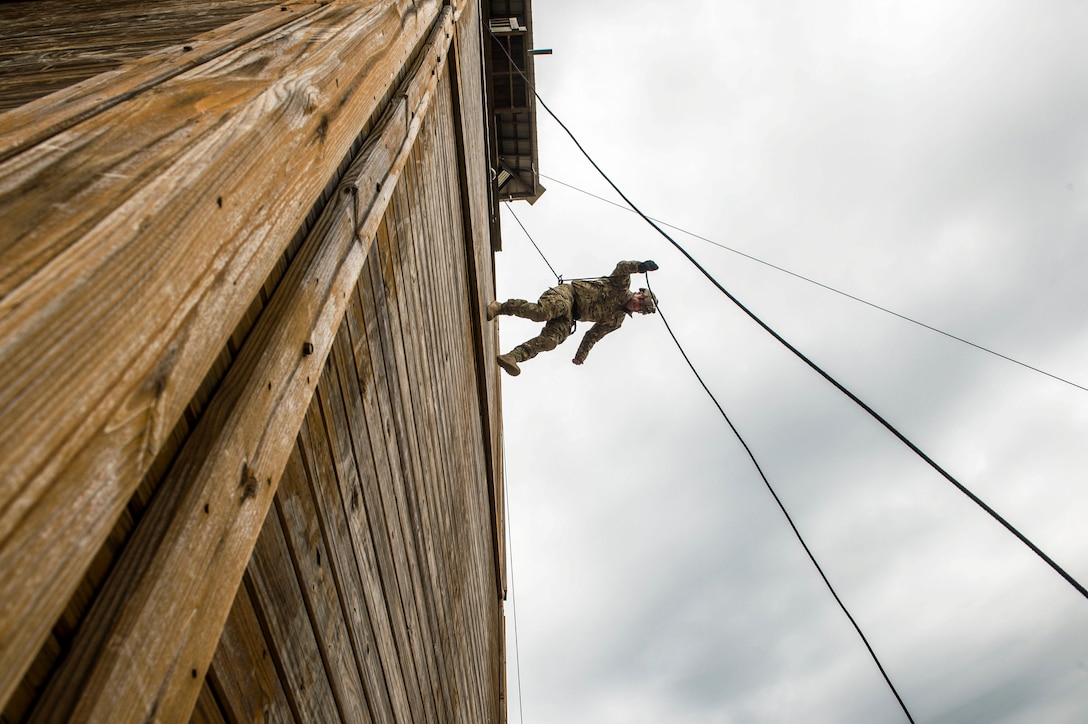 A sailor rappels from a tall building using a rope technique.