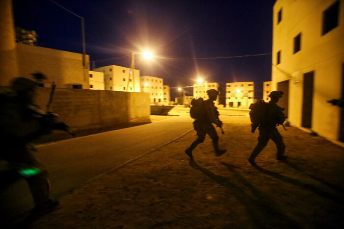 Marines run to cover during a night exercise under lights.