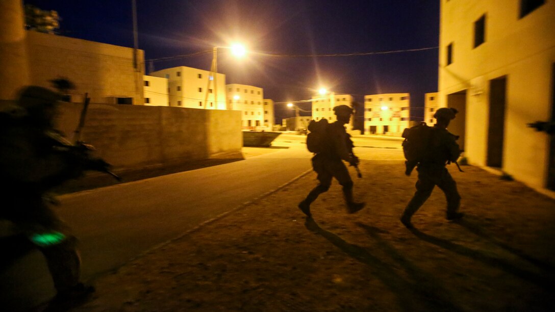 Marines run to cover during a night exercise under lights.