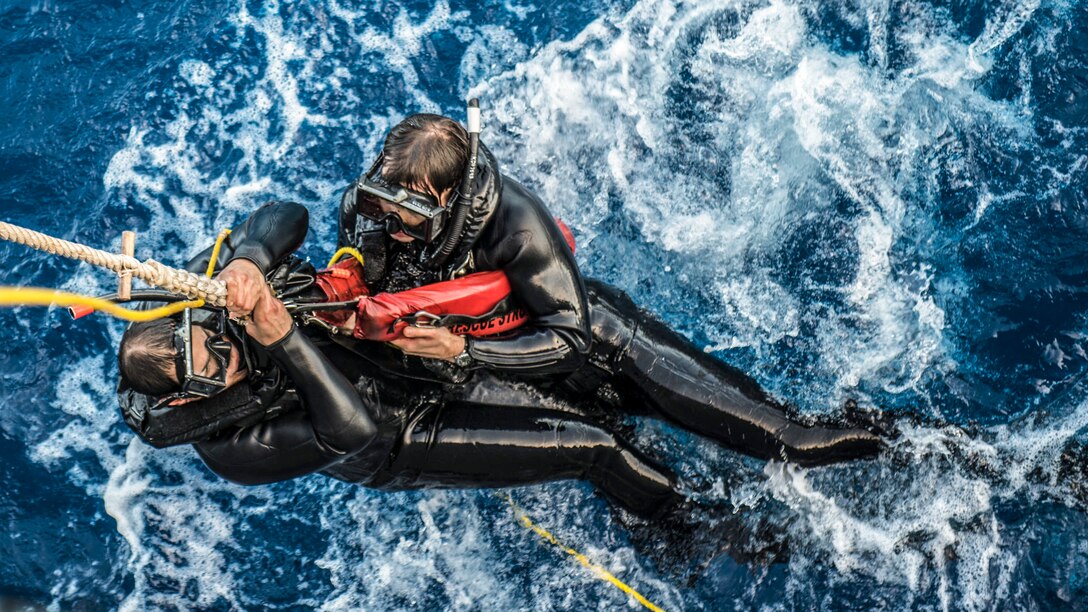 A rope hoists two sailors from the water during search and rescue swimmer training.