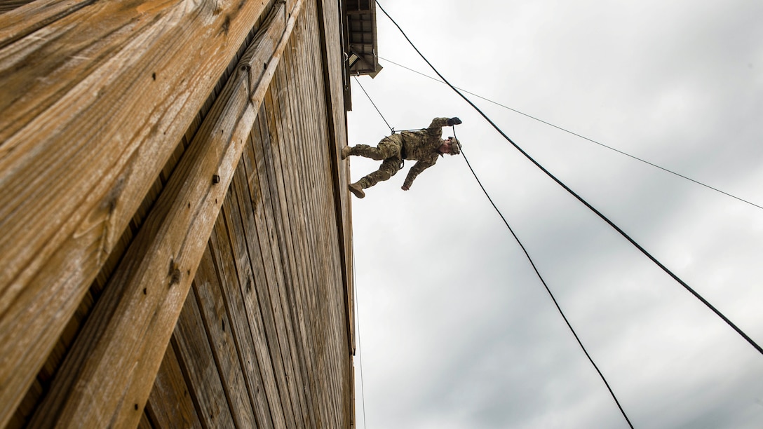 A sailor rappels from a tall building using a rope technique.