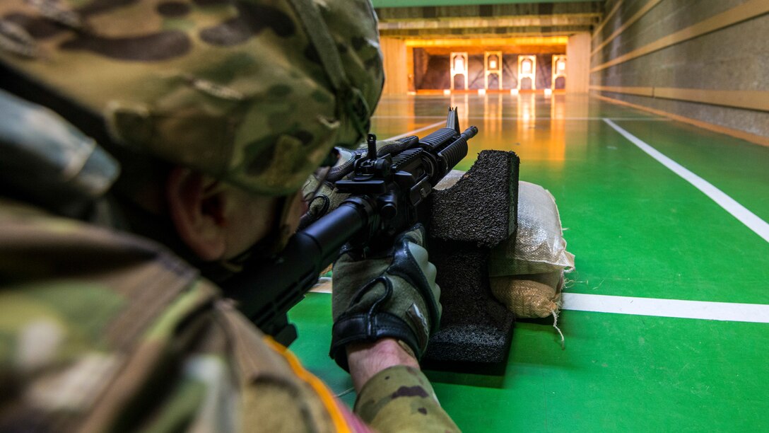 A soldier lies on a green floor as he shoots a weapon during a competition