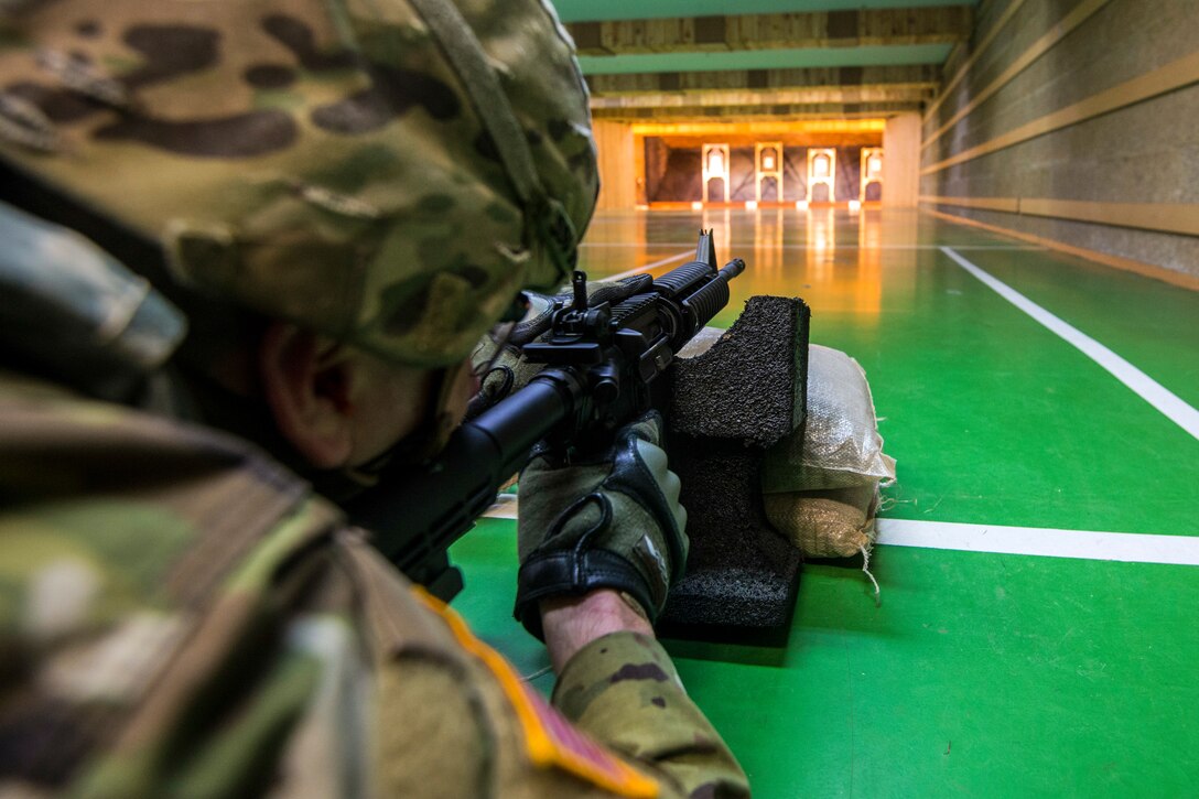 A soldier lies on a green floor as he shoots a weapon during a competition