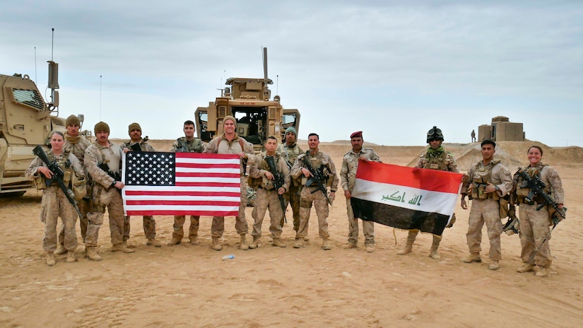 U.S. Marines and Iraqi security forces pose holding their nations' flags.