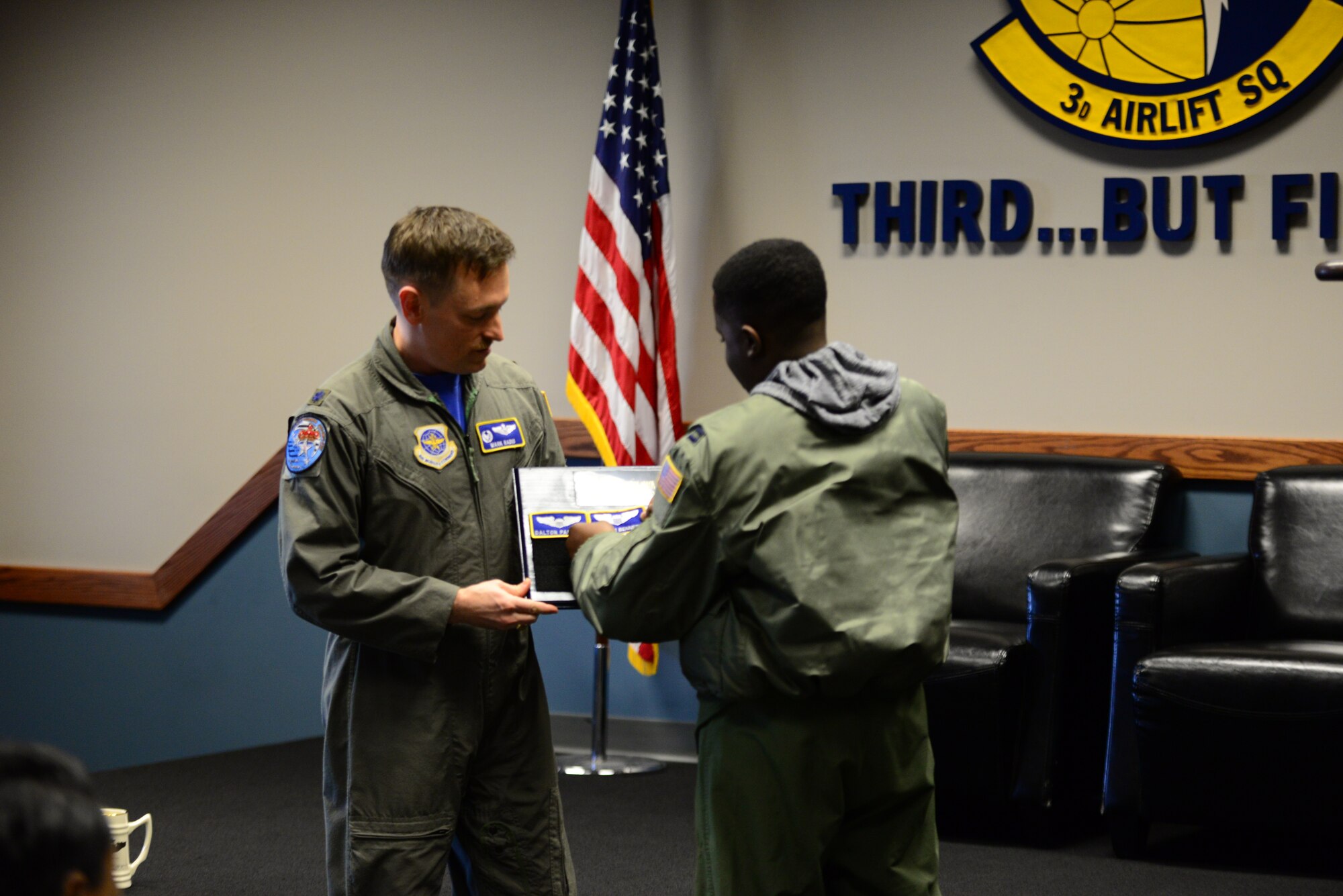 Lt. Col. Mark Radio, 3rd Airlift Squadron commander, holds the Pilot for a Day plaque while Kareem Bennett affixes his nametape to it during a squadron roll call March 16, 2018, at Dover Air Force Base, Del. Flying squadrons traditionally hold a ceremony for outgoing or retiring members that involves placing their nametape on a board to commemorate their service to the organization. (U.S. Air Force photo by Staff Sgt. Aaron J. Jenne)