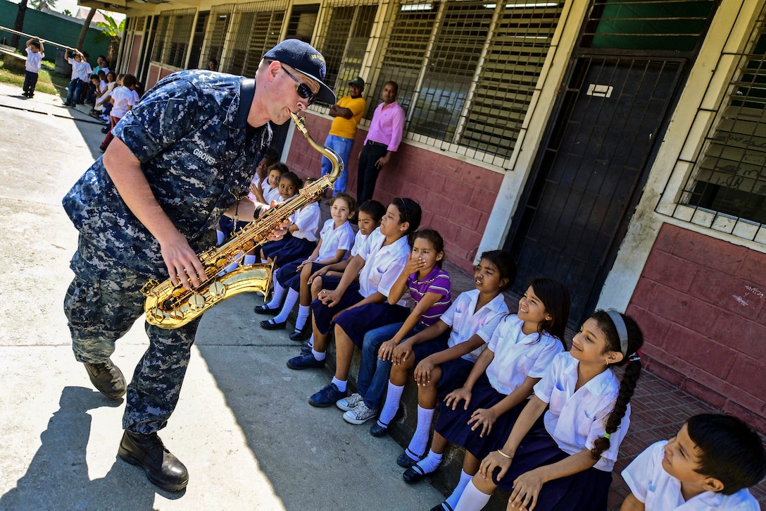 A Navy musician plays a saxophone to students at a school in Honduras.