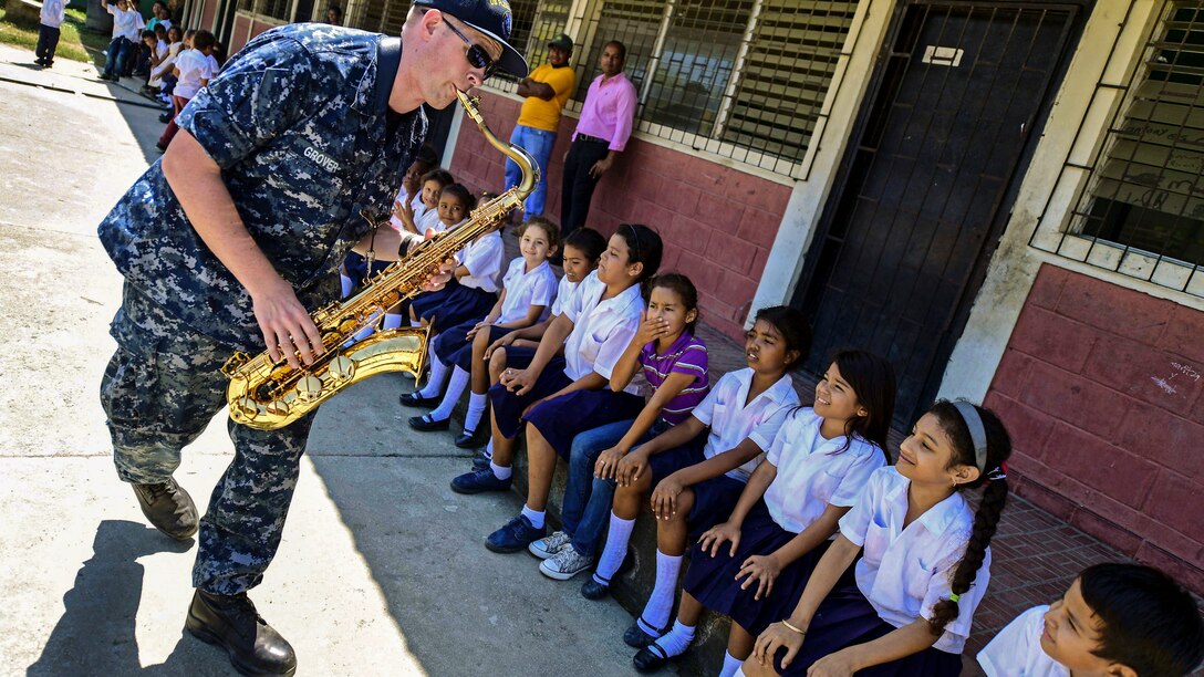 A Navy musician plays a saxophone for students.