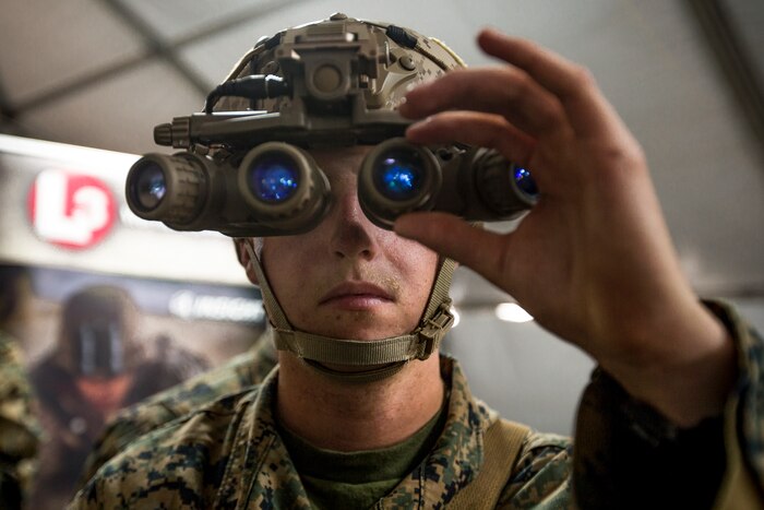 A Marine looks through an optical device with four blue lenses.