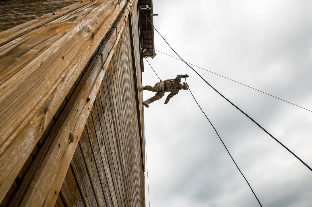 A sailor rappels from a tall building using a rope technique.