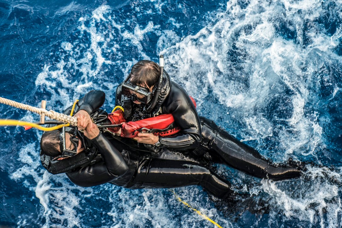 A rope hoists two sailors from the water during search and rescue swimmer training.