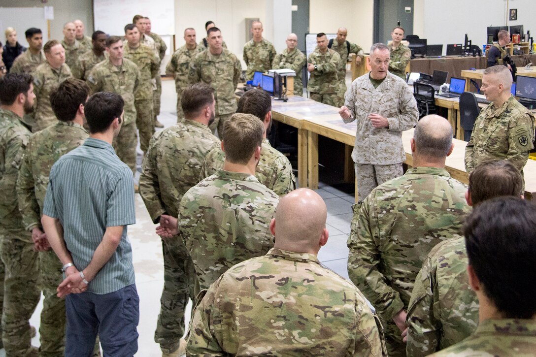 The chairman of the Joint Chiefs of Staff talks to service members standing around him.