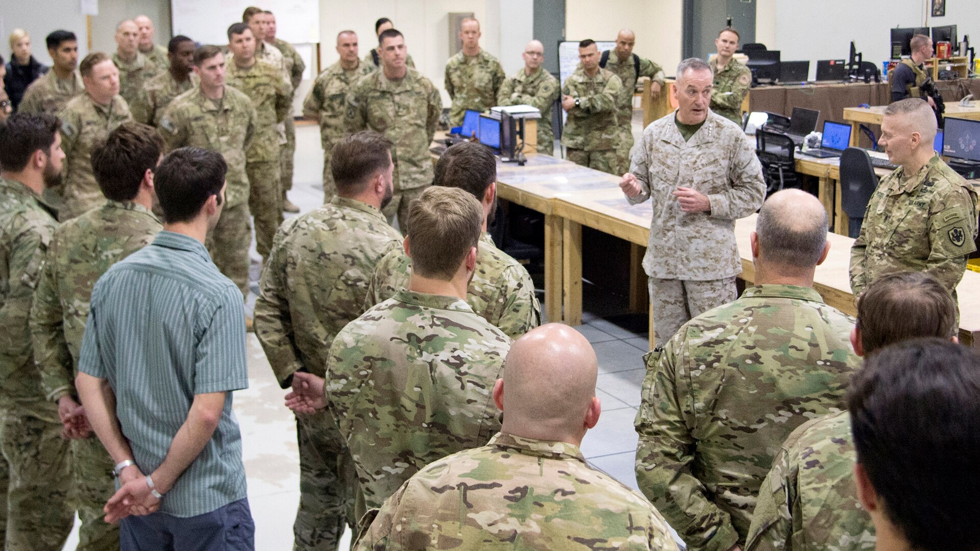 The chairman of the Joint Chiefs of Staff talks to service members standing around him.