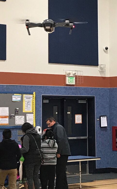A quadcopter drone, operated by members of the 9th Intelligence Squadron, hovers above students and onlookers at the Bridge Street School Career Exploration Night event in Yuba City, California, on February 20, 2018. This was the inaugural event for the school and it was attended by 51 students who had interest in the science, technology, engineering, and mathematics (STEM) career fields.