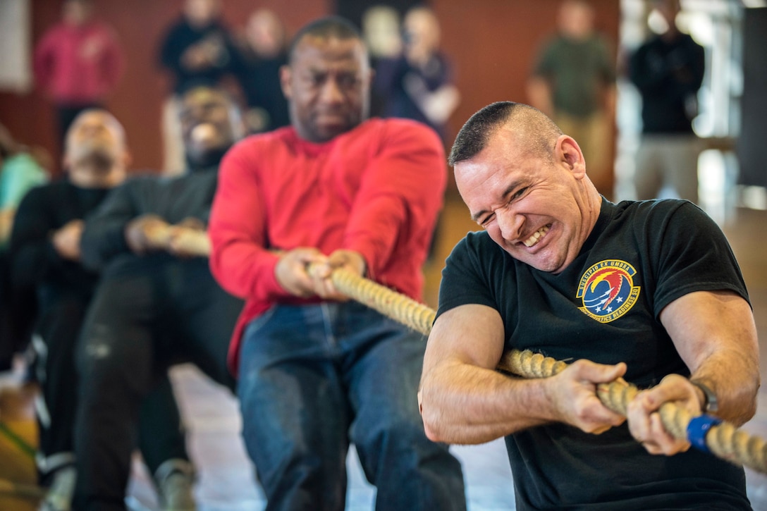 An airman pulling a rope grimaces as fellow troops help pull in the background.