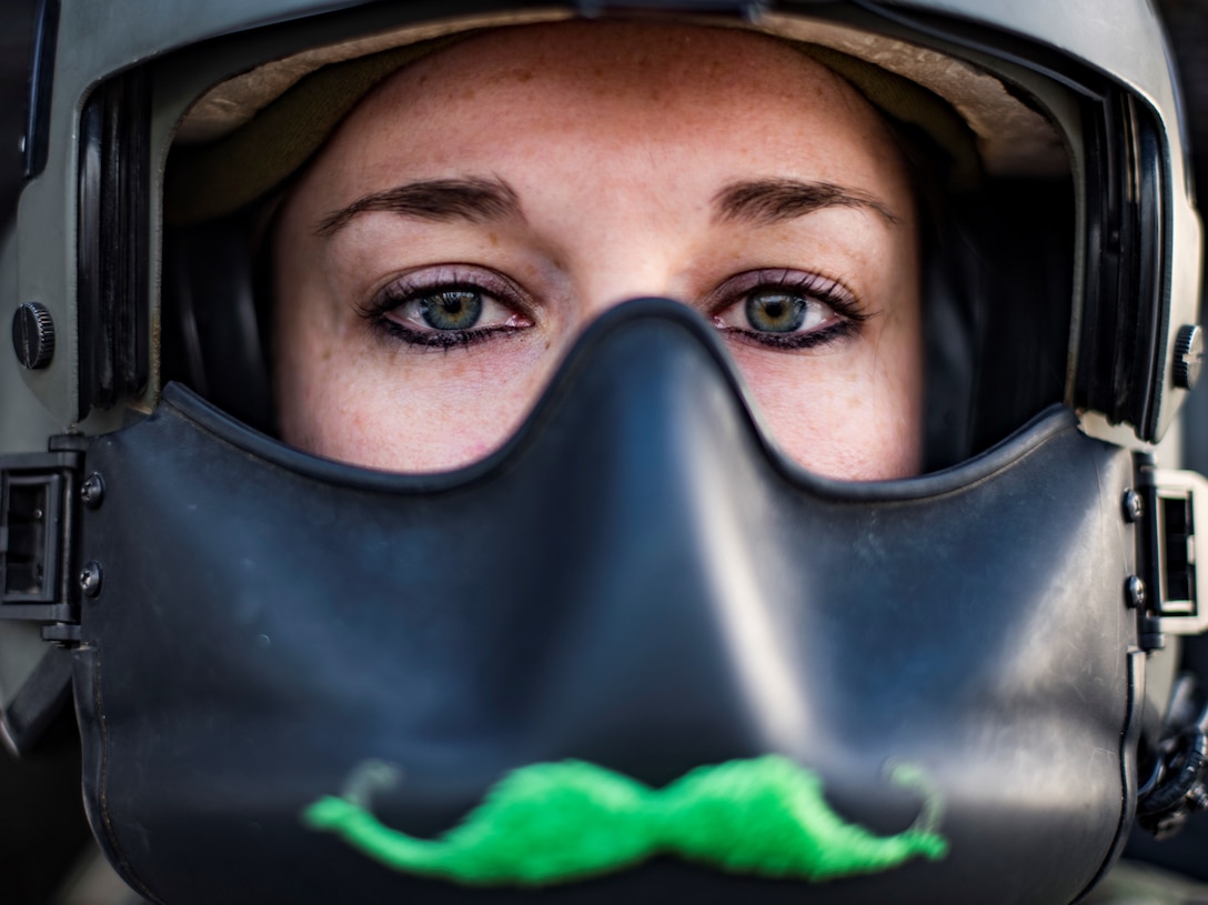 Pilot wearing a green moustache on her helmet mask poses in her aircraft.