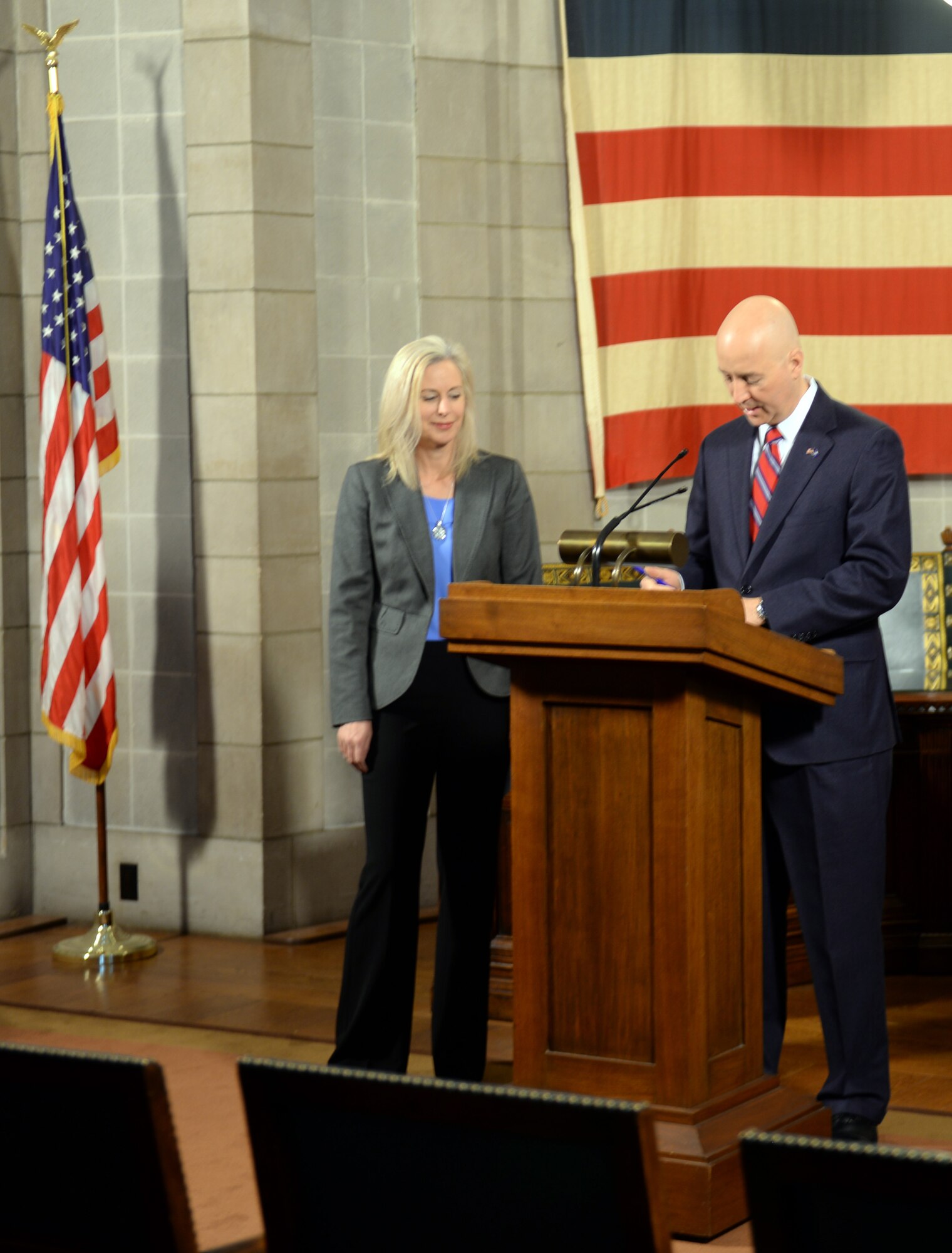 Nebraska Gov. Pete Ricketts signs a change to Rule 21, which regulates state teaching licenses, as Shannon Manion, a certified teacher and veteran school administrator as well as the spouse of Col. Michael Manion, 55th Wing commander, looks on at the Nebraska State Capitol Building in Lincoln, nebraska on March 19, 2018. Manion, along with other Offutt-based military spouses, were invited to witness the governor sign the rule change will make it easier for military spouses to teach immediately if they have recently arrived from out of state.