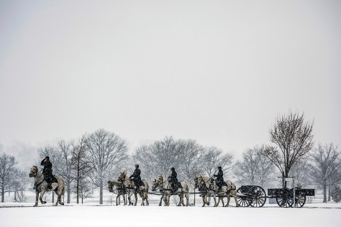 Soldiers on horseback escorting a wheeled cart proceed on a path during heavy snowfall.