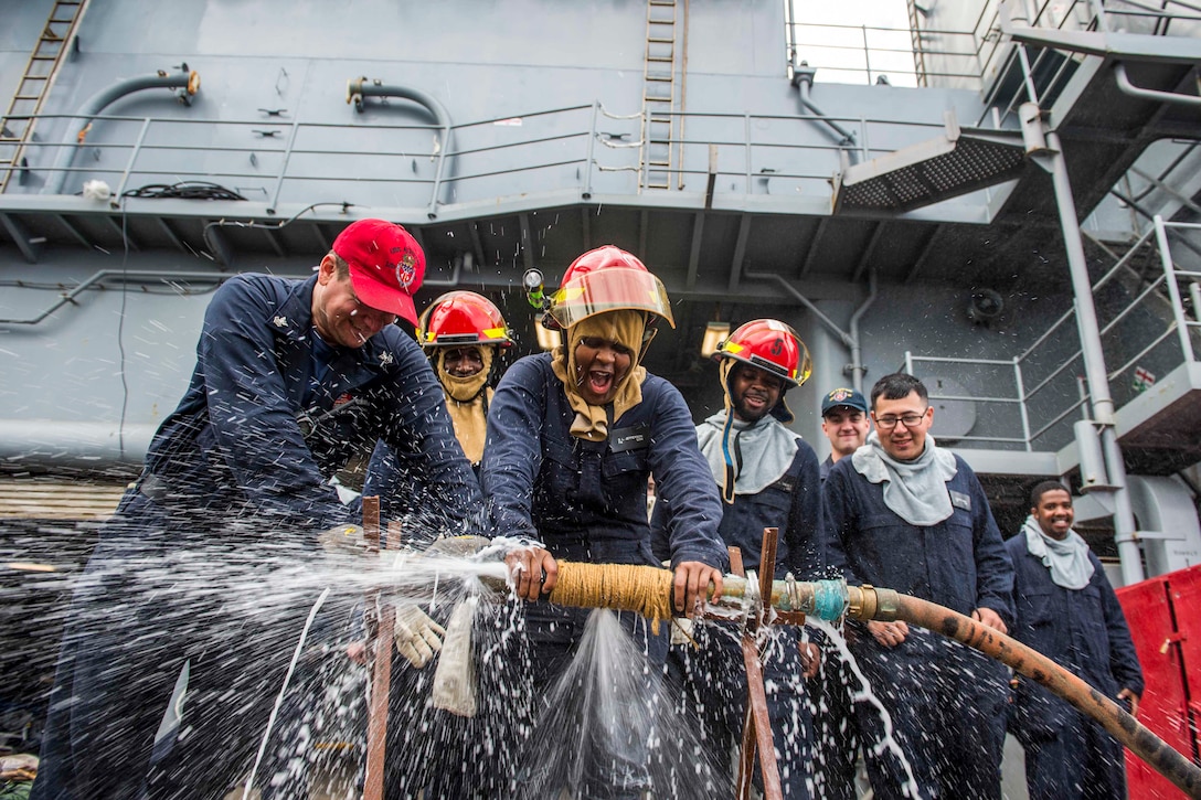 Sailors hold down a pipe to test the effectiveness of water running through it.