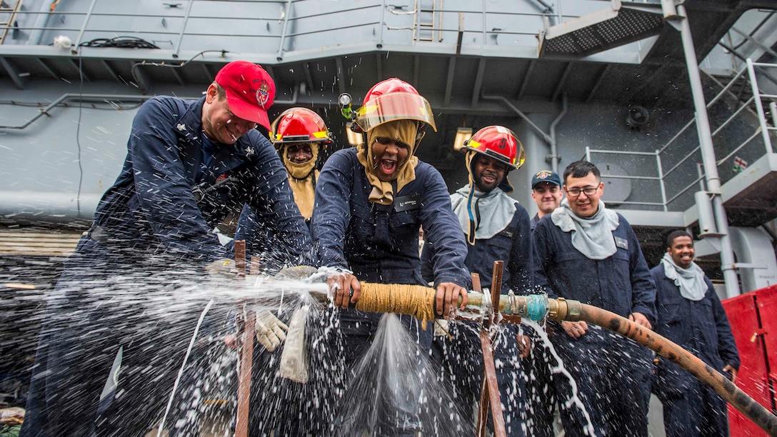 Sailors hold down a pipe to test the effectiveness of water running through it.