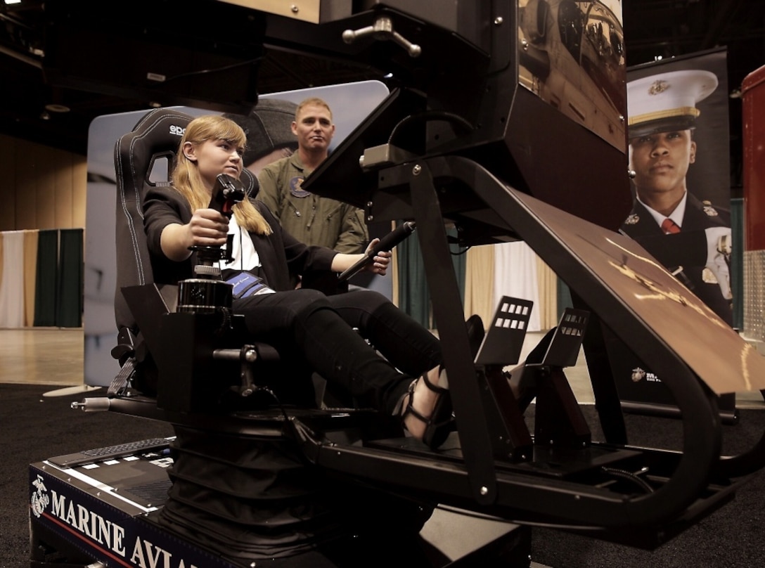 Capt. Joshua Herm assists Mary “Kate” Rourke, a student at Mountain Vista High School in Highlands Ranch, Colorado, as she pilots an AH1Z Viper flight simulator at the Women in Aviation, International 29th Annual Symposium in Reno, Nevada, March 22, 2018. Marines attended WAI to generate awareness for career opportunities in the Marines while engaging with highly-qualified individuals and key influencers.