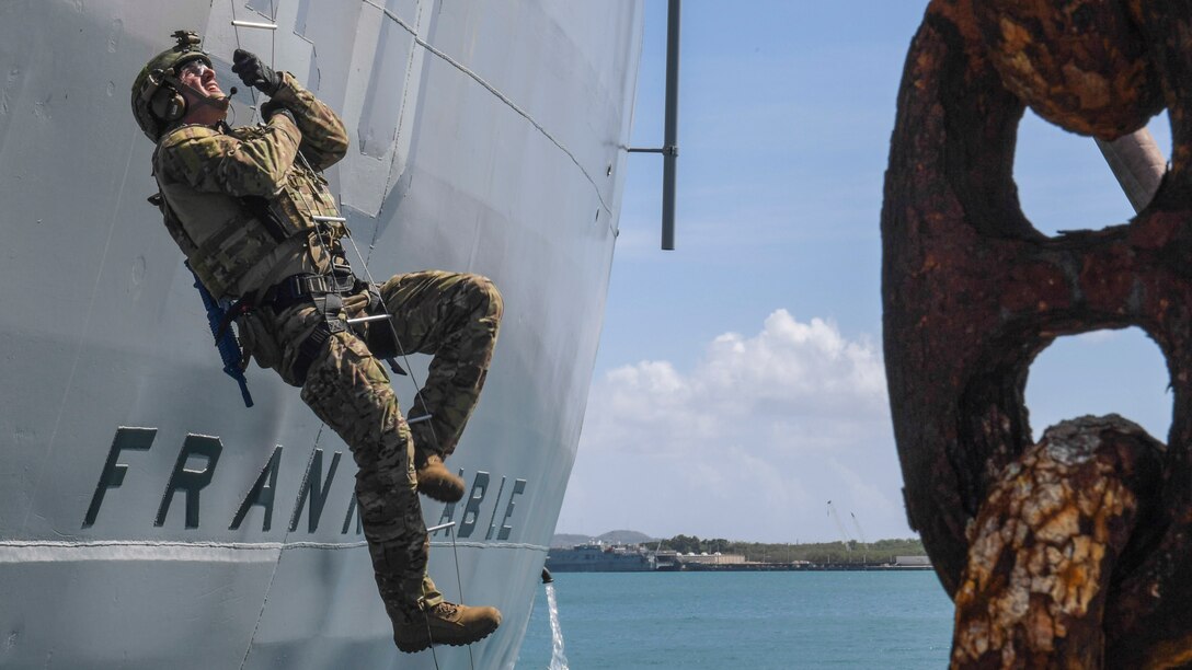 A Marine climbs a rope ladder up the side of a ship.