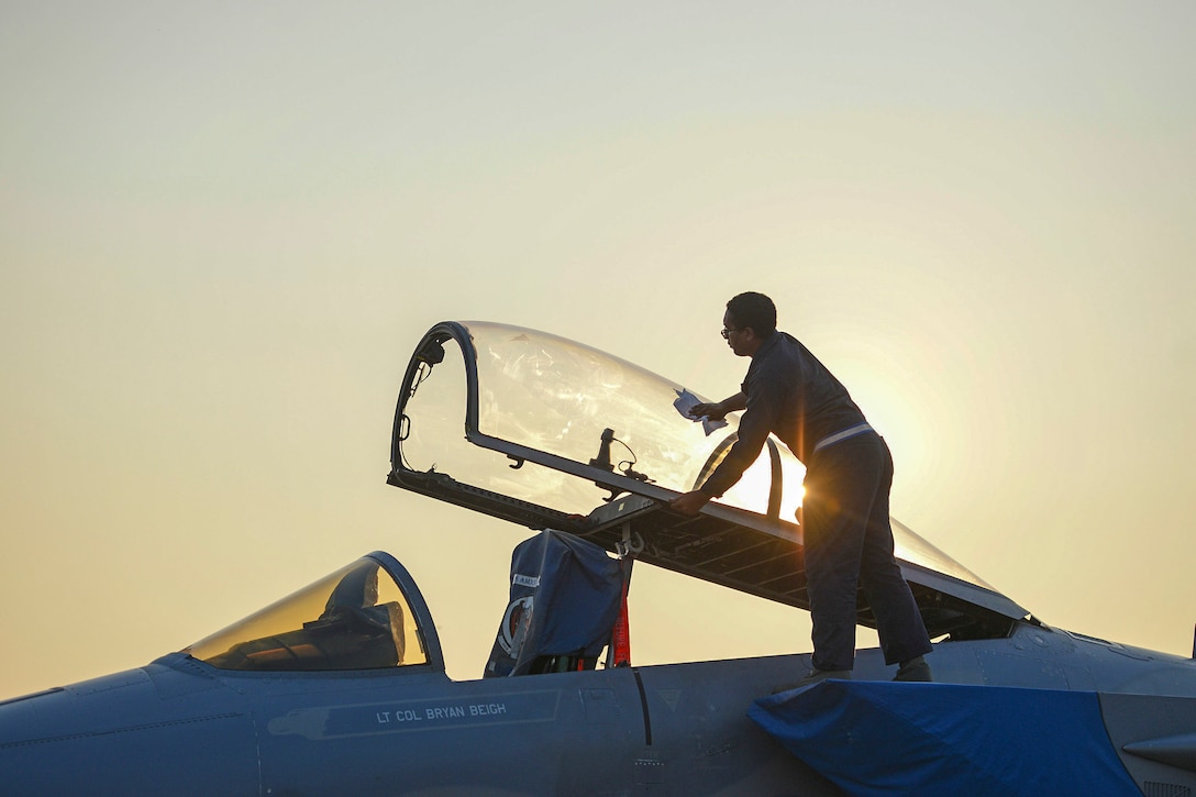 An airman wipes down an open canopy on a fighter jet.