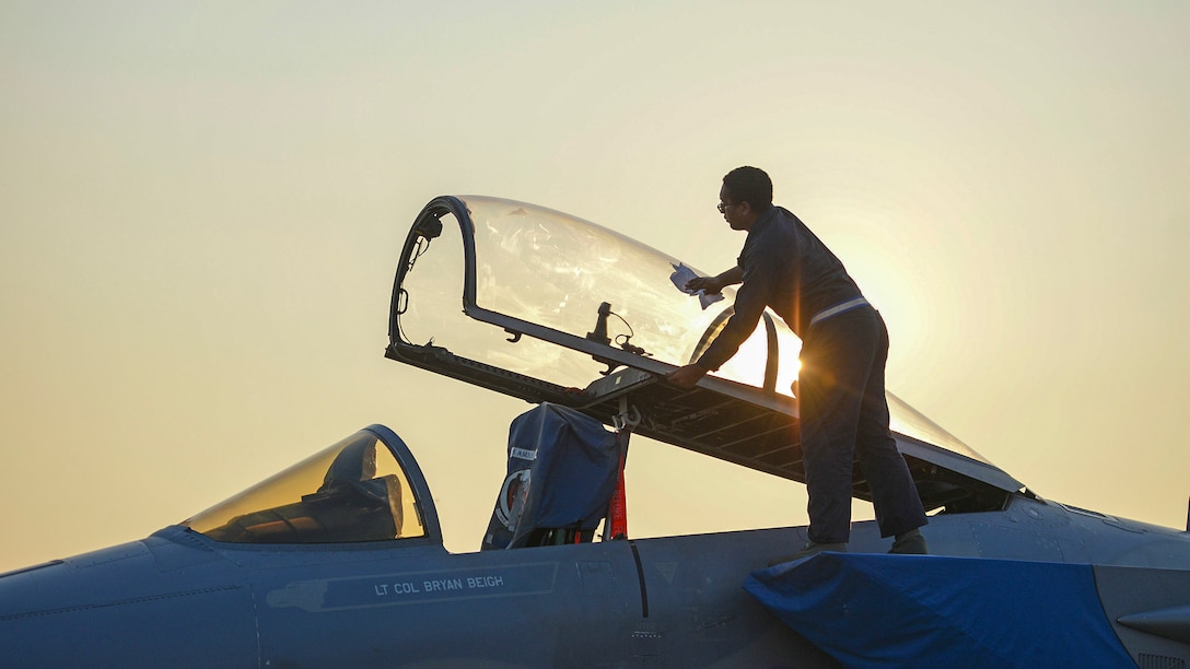 An airman wipes down an open canopy on a fighter jet.