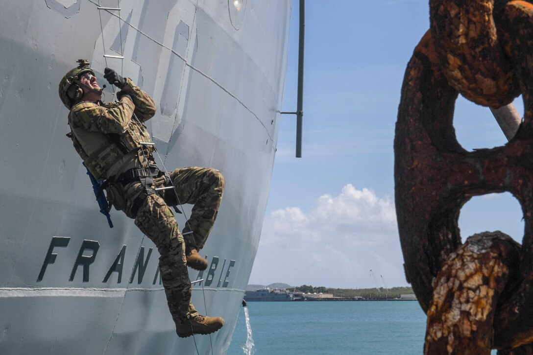 A Marine climbs a rope ladder up the side of a ship.