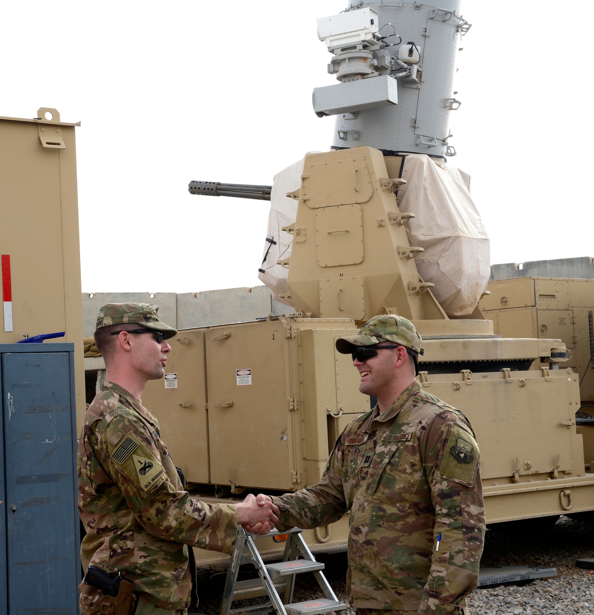 U.S. Army Capt. Eric Sylwestrak, battery commander, 2nd Battalion, 174th Air Defense Artillery Regiment, Ohio Army National Guard, shakes hands with U.S. Air Force Capt. Isaac Hoffman, project engineering officer-in-charge, 220th Engineering Installation Squadron, Ohio Air National Guard, in front of one of the Army's Counter-Rocket, Artillery, and Mortar (C-RAM) Intercept weapon systems at Kandahar Airfield, Afghanistan, March 10, 2018.