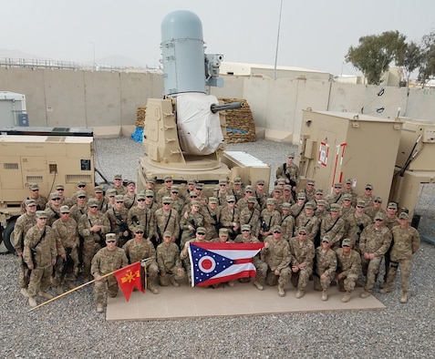 Airmen with the 220th Engineering Installation Squadron, Ohio Air National Guard, and Soldiers with the 2nd Battalion, 174th Air Defense Artillery Regiment, Ohio Army National Guard, pose for a group photo in front of one of the Army's Counter-Rocket, Artillery, and Mortar (C-RAM) Intercept weapon systems at Kandahar Airfield, Afghanistan, March 10, 2018.