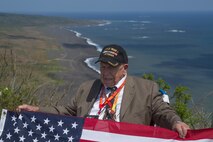 Retired Marine Cpl. Samuel “Lee” Anderson, a former member of 5th Marine Division, poses with a flag atop Mount Suribachi while explaining what he did on the island to his sons March 24, 2018 on Iwo To, Japan. Anderson who fought for 21 days on the island until a landmine, set off by another Marine, knocked him unconscious, returned to the island to participate in the 73rd Reunion of Honor. Anderson is a native of Venice, California. (U.S. Marine Corps photo by Lance Cpl. Jamin M. Powell)