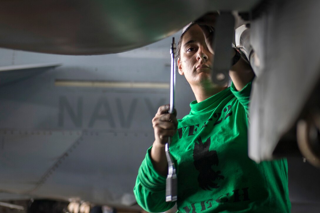 A sailor removes a panel from an aircraft.